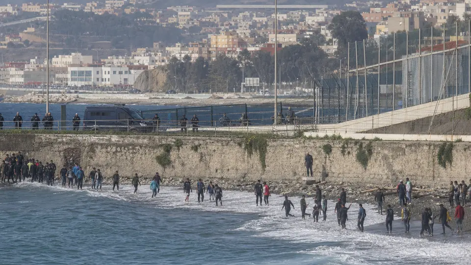 Agentes de seguridad en la valla fronteriza de Ceuta ante una concentración de personas intentando cruzar desde Marruecos.