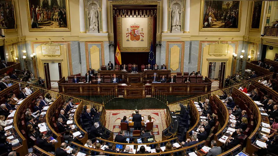 Demonstrators gathering in front of a Spanish town hall at dusk, with the flag of Ceuta displayed on the façade.