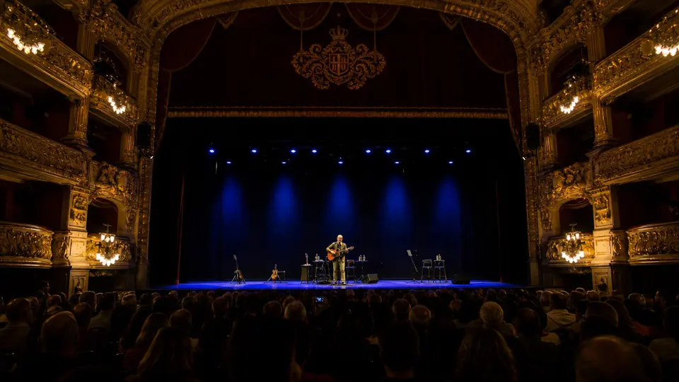 Silvio Rodríguez seated on stage at the Gran Teatre del Liceu in Barcelona, performing with a guitar during his peninsular tour opening concert.