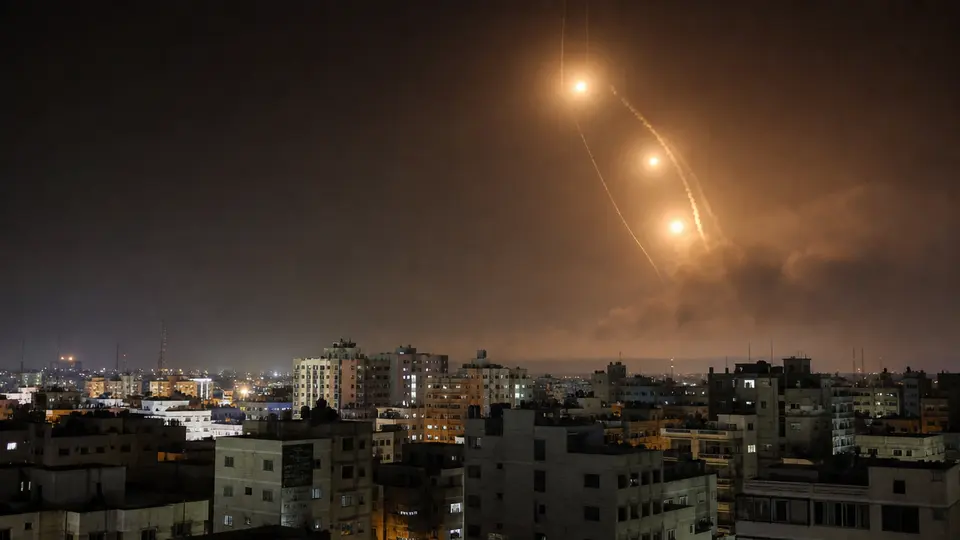 Smoke rising over an Iranian military installation following US airstrikes, with fighter aircraft visible against a night sky.
